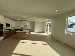 Kitchen featuring white cabinetry, a kitchen breakfast bar, recessed lighting, a kitchen island with sink, and light wood-style floors