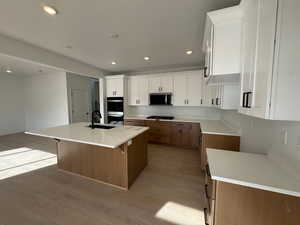 Kitchen featuring brown cabinetry, white cabinets, a kitchen island with sink, light stone countertops, and recessed lighting