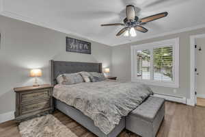 Bedroom with crown molding, a baseboard radiator, light wood-type flooring, and a ceiling fan