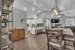 Dining area with a glass covered fireplace, lofted ceiling, wood finished floors, and a ceiling fan