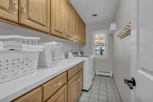 Laundry area featuring light tile patterned flooring, baseboard heating, cabinet space, and washing machine and clothes dryer
