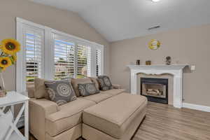 Living room with vaulted ceiling, a tiled fireplace, and light wood-style flooring