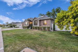 Ranch-style house with roof mounted solar panels, a front lawn, brick siding, a garage, and concrete driveway