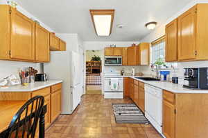 Kitchen featuring light countertops, white appliances, and brown cabinets