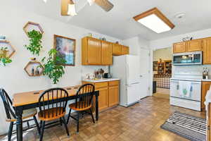 Kitchen with white appliances, light countertops, brick patterned floors, and brown cabinets