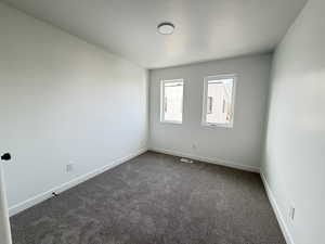 Spare room featuring dark colored carpet and baseboards