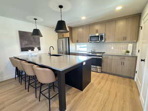 Kitchen featuring backsplash, stainless steel appliances, a breakfast bar area, decorative light fixtures, and light wood-type flooring