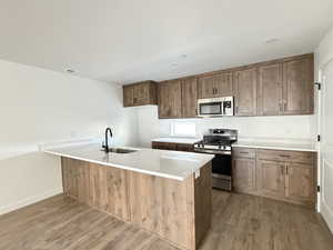 Kitchen with a peninsula, appliances with stainless steel finishes, dark wood finished floors, light stone counters, and brown cabinetry