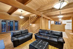 Living room with stairs, log walls, light wood-type flooring, and a wood ceiling with exposed beams