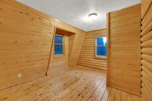 Bonus room featuring a textured ceiling, rustic walls, hardwood / wood-style floors, and wood walls