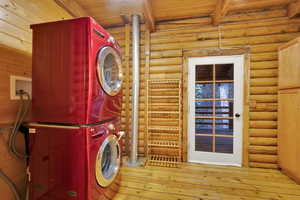 Laundry area with wood-type flooring, stacked washer and clothes dryer, wood ceiling, and rustic walls