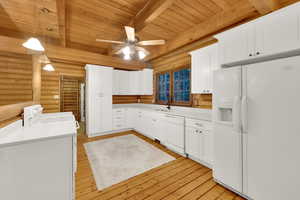 Kitchen with white appliances, light wood-style flooring, a wooden ceiling with exposed beams, white cabinetry, and light countertops