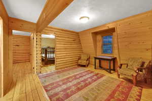 Living area featuring light wood finished floors, beam ceiling, a textured ceiling, and log walls