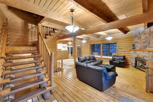 Living room featuring stairs, a fireplace, light wood finished floors, log walls, and a wood ceiling with exposed beams