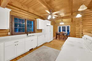 Kitchen featuring white cabinets, log walls, hanging light fixtures, light countertops, and a ceiling fan