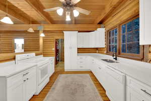 Kitchen featuring white appliances, decorative light fixtures, white cabinets, light wood finished floors, and a wood ceiling with exposed beams