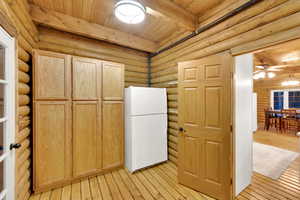 Kitchen featuring freestanding refrigerator, rustic walls, light brown cabinetry, light wood-style floors, and a wood ceiling with exposed beams