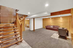 Living area with wooden walls, recessed lighting, light carpet, and stairs