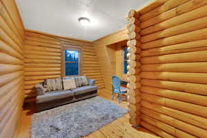Living area with a textured ceiling, light wood-style flooring, and log walls