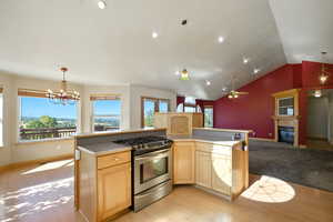 Kitchen with light brown cabinetry, stainless steel gas stove, a glass covered fireplace, light countertops, and recessed lighting