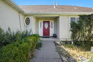 View of exterior entry featuring roof with shingles and stucco siding
