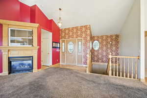 Unfurnished living room featuring high vaulted ceiling, light carpet, a glass covered fireplace, and wallpapered walls