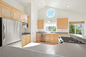 Kitchen featuring appliances with stainless steel finishes, light brown cabinets, high vaulted ceiling, and light countertops