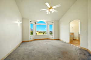 Empty room featuring carpet, high vaulted ceiling, arched walkways, and a ceiling fan