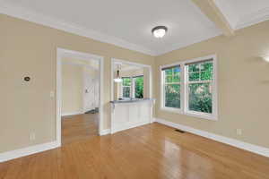 Unfurnished room featuring crown molding, light wood finished floors, and beamed ceiling