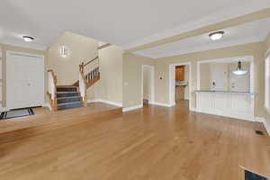 Unfurnished living room with crown molding, light wood finished floors, and stairway