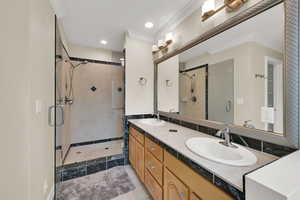 Bathroom featuring double vanity, a shower stall, crown molding, and recessed lighting