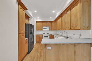 Kitchen with a peninsula, backsplash, white appliances, light countertops, and light wood-type flooring