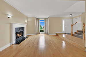 Unfurnished living room with crown molding, stairway, light wood finished floors, and a fireplace