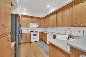 Kitchen featuring decorative backsplash, white appliances, light wood-style flooring, and recessed lighting