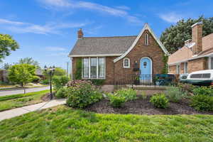 Tudor house with brick siding, a chimney, a front yard, and roof with shingles