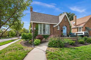 Tudor home featuring a shingled roof, a front lawn, a chimney, and brick siding