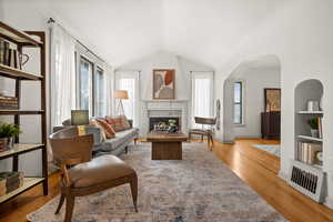 Living area with plenty of natural light, light wood-type flooring, a fireplace, arched walkways, and lofted ceiling