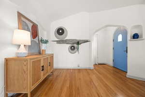 Foyer with arched walkways, light wood-type flooring, and lofted ceiling