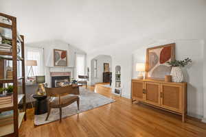 Living area featuring light wood-style flooring, arched walkways, vaulted ceiling, and a glass covered fireplace