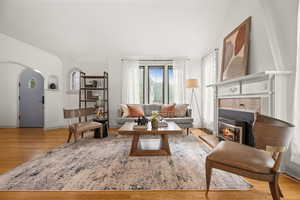 Living area with arched walkways, light wood-style floors, and a glass covered fireplace