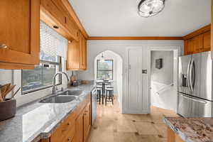Kitchen featuring appliances with stainless steel finishes, light stone countertops, ornamental molding, brown cabinetry, and arched walkways