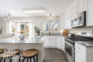 Kitchen featuring appliances with stainless steel finishes, a kitchen breakfast bar, white cabinetry, and light stone counters