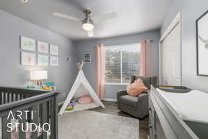 Bedroom with a nursery area, dark wood-type flooring, a ceiling fan, and a closet