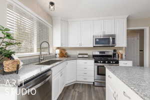 Kitchen with white cabinets, stainless steel appliances, light stone counters, and new LPV flooring