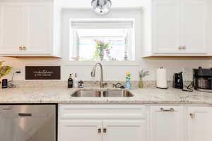 Kitchen featuring stainless steel dishwasher, light stone counters, and white cabinets