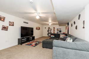 Carpeted living room featuring ceiling fan and baseboards