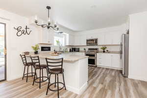Kitchen with decorative light fixtures, a breakfast bar area, stainless steel appliances, and white cabinetry