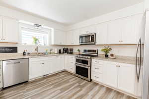 Kitchen with appliances with stainless steel finishes, light stone counters, and white cabinets
