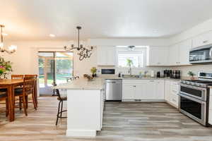 Kitchen with appliances with stainless steel finishes, a chandelier, light wood-type flooring, white cabinets, and a kitchen bar