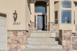 Entrance to property featuring stone siding, a garage, and stucco siding